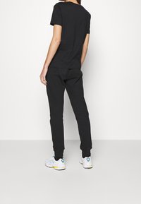 Camiseta de algodón negra de manga corta y pantalones de chándal negros a juego. Zapatillas blancas con detalles en verde y amarillo que completan el atuendo.