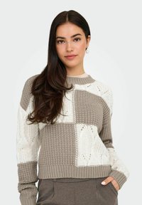 Maglione lavorato a maglia con un design cropped; presenta un patchwork di texture beige e bianche, inclusi motivi a treccia e a cesto, con polsini a coste.