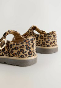 Chaussures en imprimé léopard beige avec des taches noires et marron. Dotées d'un bout fermé, d'une sangle ajustable et d'une semelle en caoutchouc gris solide.