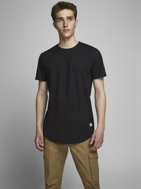 Camiseta negra de manga corta con cuello redondo, hecha de algodón. Presenta un dobladillo curvado y una pequeña etiqueta blanca en la parte inferior izquierda.