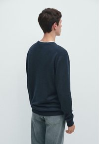 Granatowy sweter z długimi rękawami, okrągłym dekoltem i ściągaczami na mankietach, zestawiony z jasnoszarymi jeansami z denimu. Prosty, nieozdobiony design.