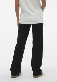 Calças largas pretas feitas de tecido macio, com um corte descontraído e uma textura suave, combinadas com uma camisa justa de cor clara.