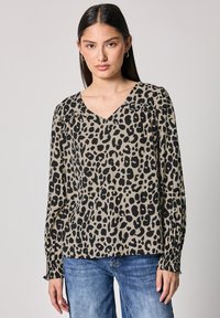 Blusa a stampa leopardata con scollatura a V, maniche lunghe con polsini arricciati e un tessuto leggero e testurizzato. I colori principali sono beige e nero.