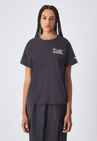 Camiseta de algodón negra con mangas cortas, que presenta "Champion" y "Un Mejor Mañana" impresos en blanco en la zona del pecho.