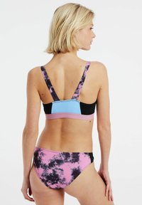 Mnohobarevný bikiny set s designem v černé, modré a růžové. Vrchní díl má široká ramínka a barevně blokovaný vzor; spodní díl ukazuje efekt tie-dye v růžové a černé.