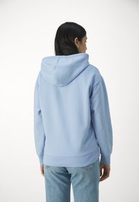 Felpa con cappuccio azzurro chiaro dal taglio morbido, dotata di un cappuccio ampio, polsini a coste e un design della schiena senza cuciture. Indossata con jeans azzurri chiari.