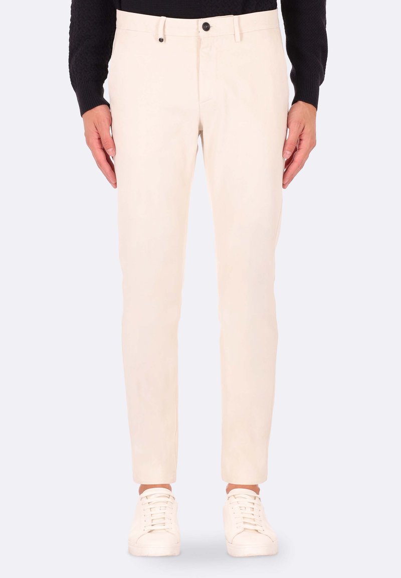Pantaloni in cotone beige a taglio slim, con chiusura a bottone e due tasche frontali, abbinati a sneaker bianche.