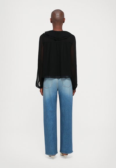 Zwarte doorschijnende blouse met lange mouwen en rimpelcollar, gecombineerd met high-waisted, wijde lichtblauwe jeans met een gradient fade.