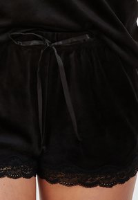 Schwarze Samtshorts mit einem satinierten Kordelzugbund, ausgestattet mit einem gewellten Spitzenbesatz am Saum für zusätzlichen Textur und Details.