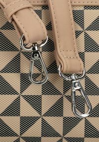 Bolso de patrón geométrico en beige y negro con asas lisas y herrajes plateados, que presenta ganchos de presión y un diseño triangular texturizado.