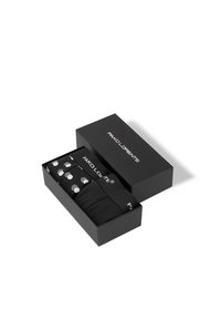 Zestaw trzech skarpetek w czarnym pudełku. Dwie jednolite czarne, jedna czarna w białe kropki. Pudełko z białym logo marki i prostymi liniami.