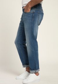 Vaqueros de mezclilla con un lavado azul medio, diseño de pierna recta, ligero desvanecimiento y puños enrollados, combinados con zapatillas blancas.