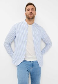 Camicia a righe blu e bianche con colletto alla coreana, in tessuto leggero, e una tasca sul petto, indossata sopra una t-shirt bianca e jeans blu.