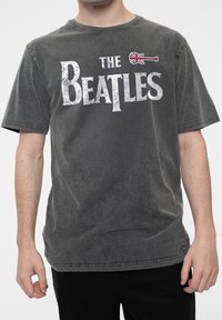 Gray cotton t-shirt featuring "THE BEATLES" in bold white text. Includes a small British flag graphic. Short sleeves, relaxed fit, smooth texture.