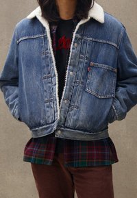 Jeansjacka med faux fur-krage, sten-tvättad blå, framficka och silverknappar. Lager på en grön och röd rutig skjorta.