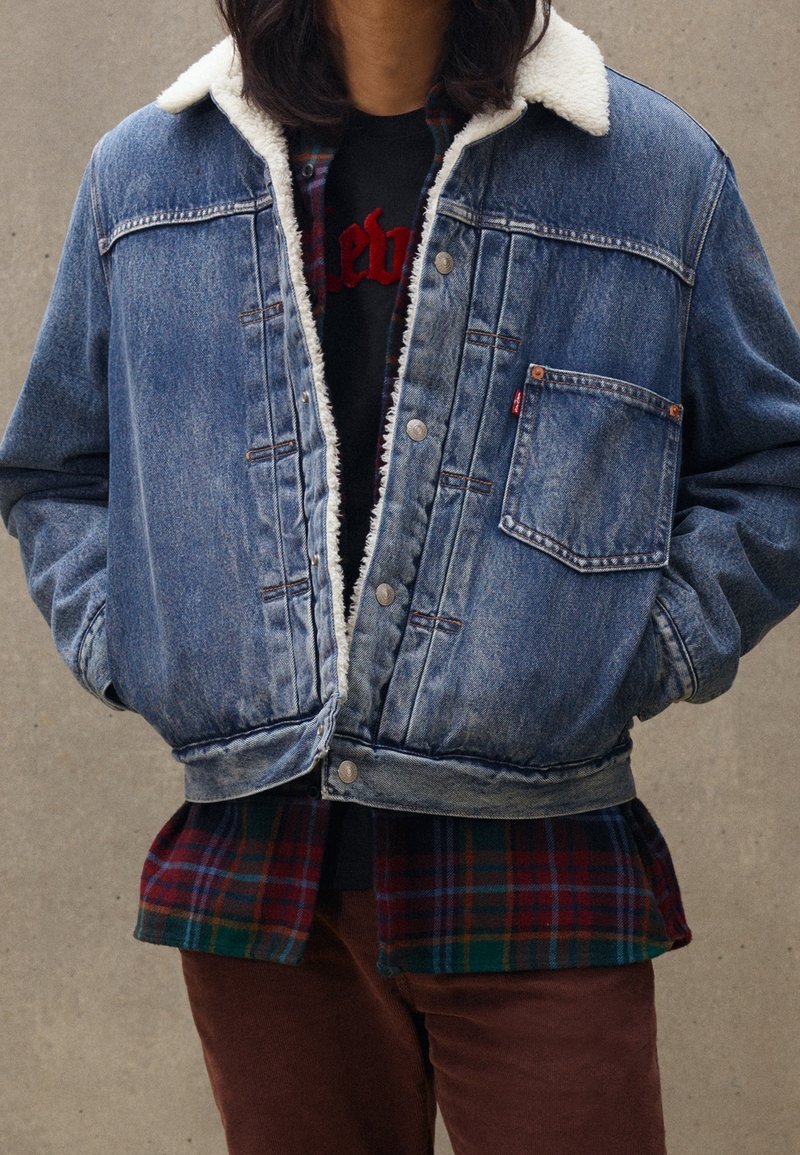 Jeansjacka med faux fur-krage, sten-tvättad blå, framficka och silverknappar. Lager på en grön och röd rutig skjorta.