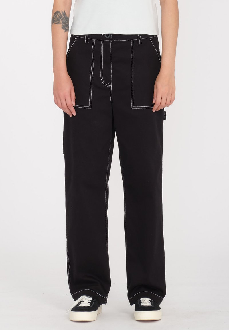 Pantaloni neri a gamba larga con cuciture bianche a contrasto, tasche frontali e chiusura con bottone. Indossati con sneakers nere e bianche.