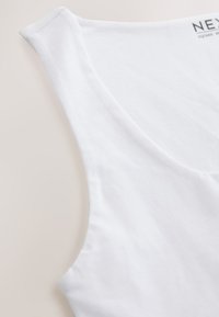 Fehér, széles pántos, ujjatlan pamut trikó közeli kép, mély nyakkivágással, bézs háttéren.