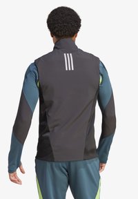 Chaqueta deportiva negra con acentos azules y verdes, con un cuello alto y tres franjas blancas en la parte posterior. Ajuste slim y mangas largas.