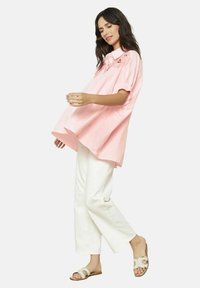Camicia oversize a quadri rosa con colletto e motivo floreale ricamato, indossata con pantaloni bianchi a gamba larga e sandali beige.