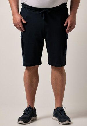 Man draagt zwarte cargoshorts met koord en zwarte sport schoenen, staand tegen een effen achtergrond.