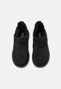 Fekete velúr Skechers slip-on cipők párja, bolyhos béléssel és varrott részletekkel, felülnézetből, fehér háttér előtt.