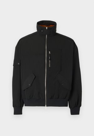 Zwarte jas van lichtgewicht stof, met een hoge kraag, rits aan de voorkant, borstzak en twee voorzakken met flap en drukknoopsluiting.