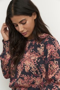 Blouse à manches longues en tissu noir avec des motifs circulaires roses et pêche. Texture douce avec des détails froncés aux poignets.
