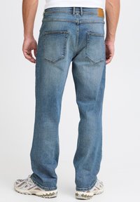 Lyseblå denimjeans med rett ben, med to baklommer og en brun skinnlapp på midjebeltet.