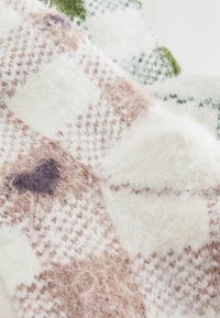 Wielokolorowy dziergany koc z jasnoróżowymi, białymi i zielonymi łatami, charakteryzujący się miękką, puszystą teksturą i wzorem w kratę.