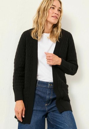 Black knitted cardigan with an open front, textured pattern, ribbed cuffs, and two pockets, worn over a white shirt and blue jeans.
