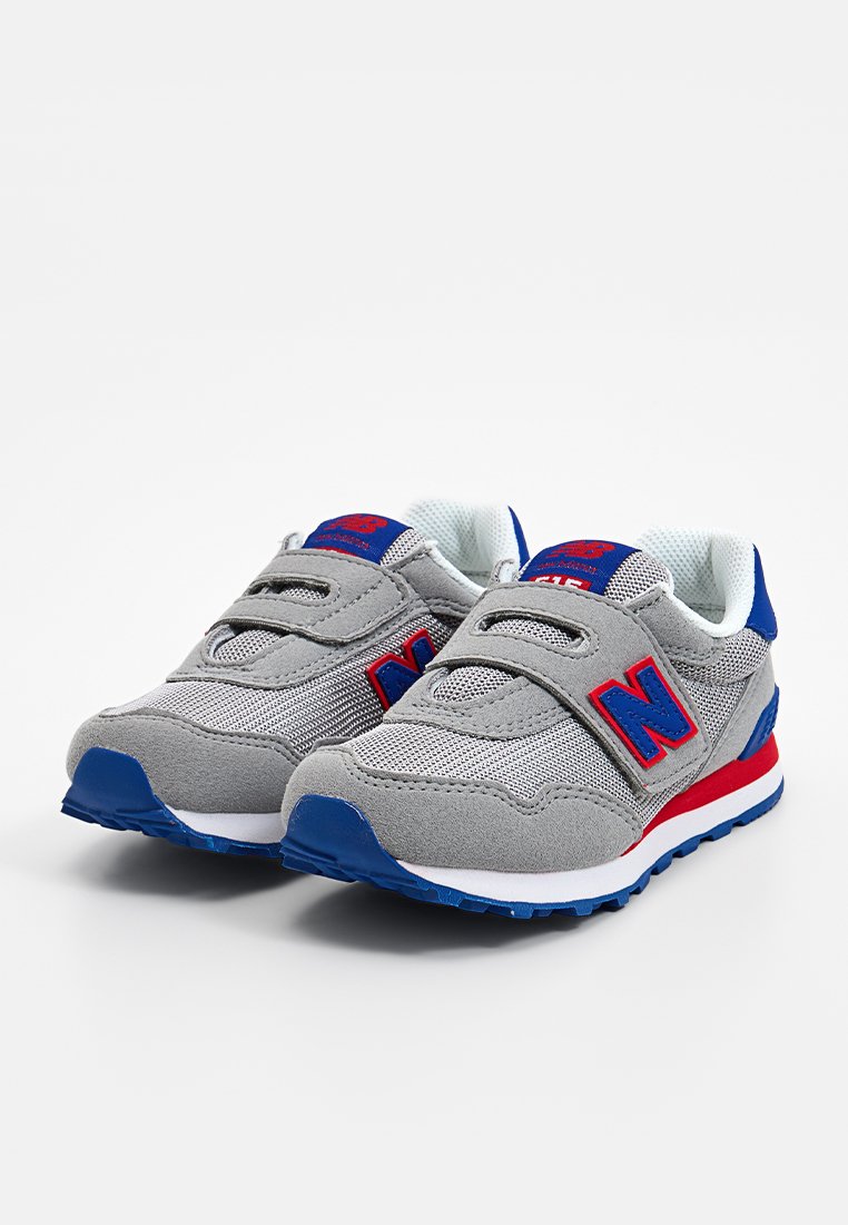 Baskets de sport grises en matériaux en mesh et en suède. Présentent un logo "N" rouge, des accents bleus et une sangle à velcro. Semelle en caoutchouc pour adhérence.