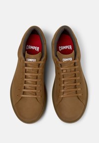 Sneakers in pelle marrone con punta rotonda, lacci piatti e soletta rossa. Logo visibile sulla linguetta e sulla soletta, superficie texturizzata e design semplificato.