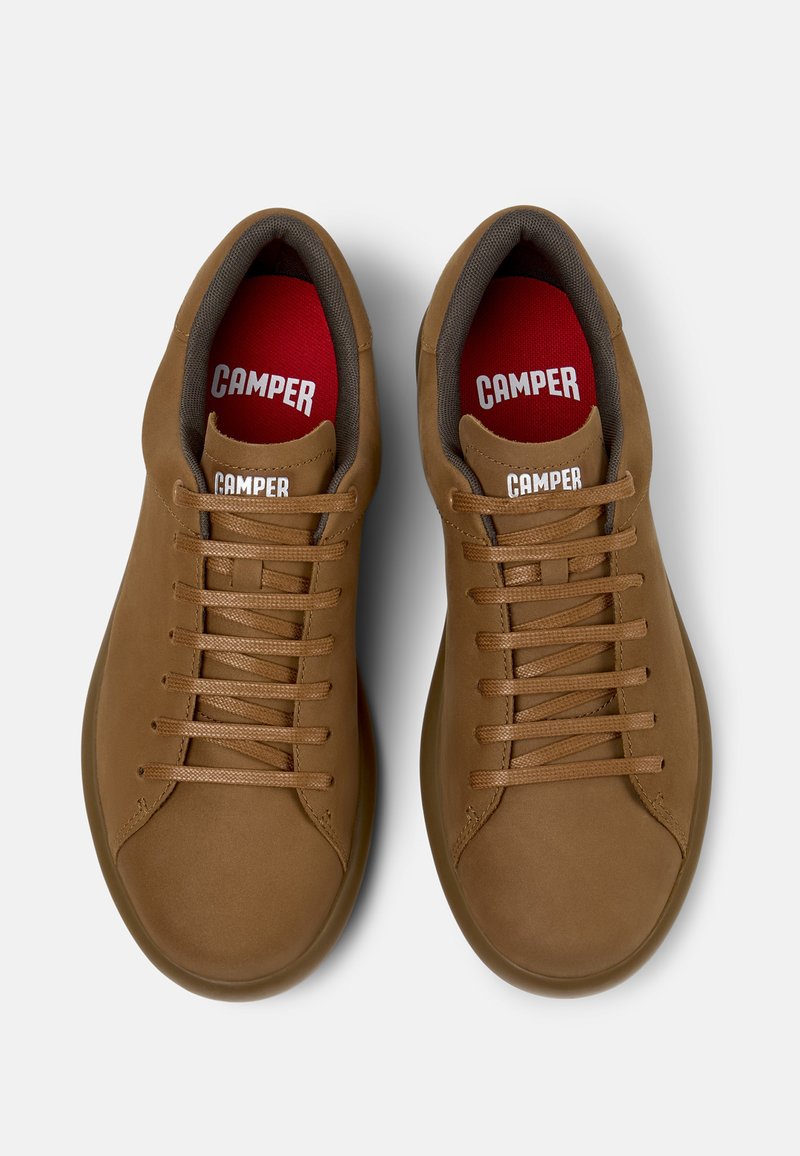 Bruna lädersneakers med rund tå, platta snören och röda innersulor. Logga som visas på tungan och innersulan, texturerad yta och förenklad design.
