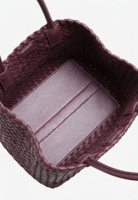 Βαθύ μοβ υφασμένη δερμάτινη τσάντα tote με λείο δερμάτινο πάτο και δύο στρογγυλεμένες λαβές σε λευκό φόντο.
