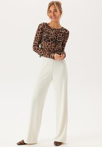 Långärmad topp med leopardmönster, ihop med vida vita byxor. Toppen har rund hals och knappdetaljer.