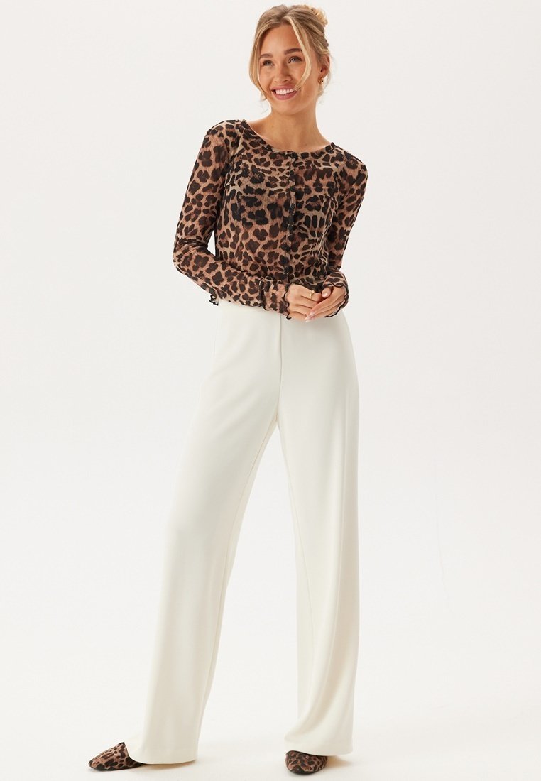 Långärmad topp med leopardmönster, ihop med vida vita byxor. Toppen har rund hals och knappdetaljer.