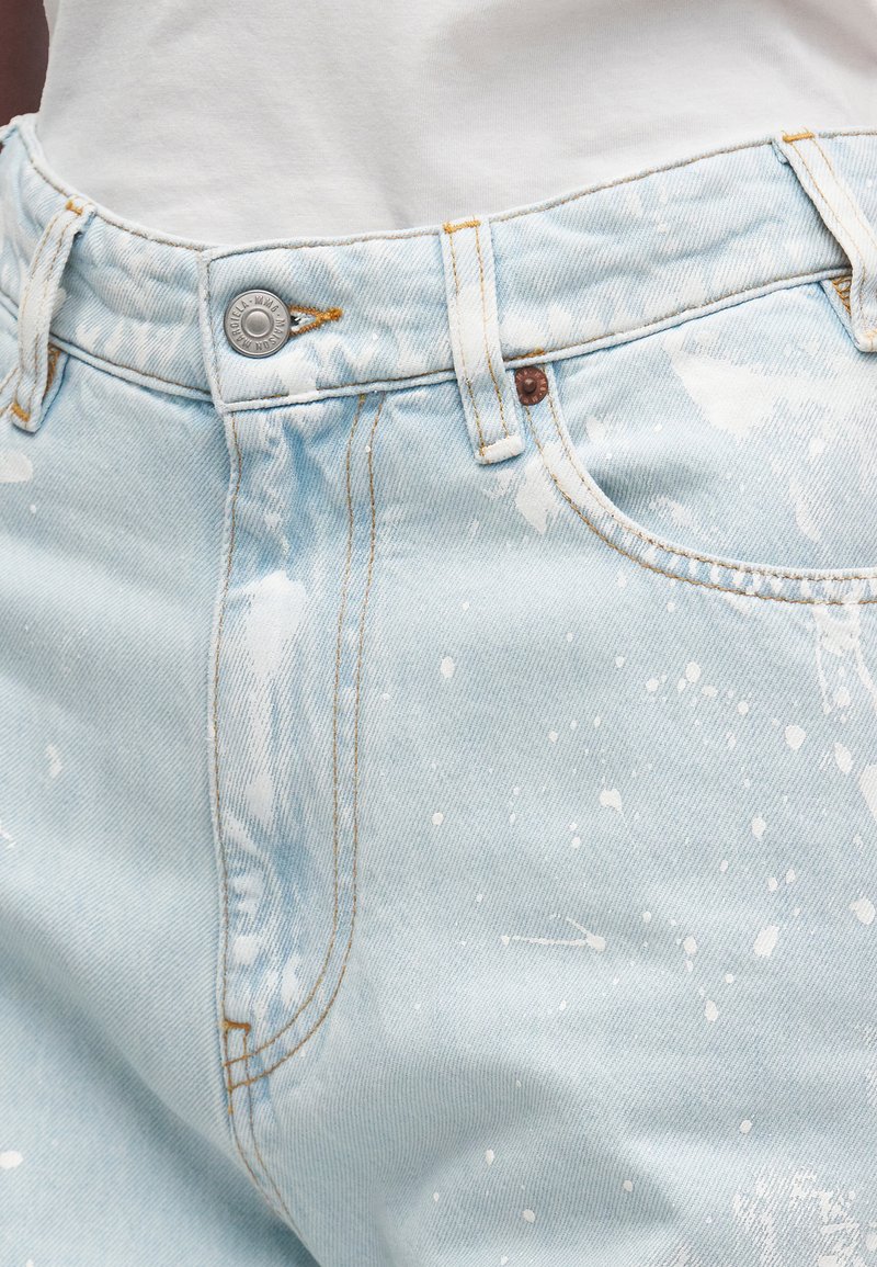 Lichtblauwe denim jeans met wit verfspetterpatroon, metalen knoop, voorzak en zichtbare stiksels op de tailleband.