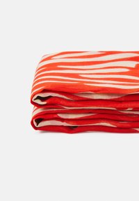 Tissu léger plié avec des rayures zébrées rouges et beiges sur un fond blanc uni.