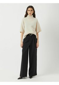 Světle béžový pletený svetr s rolákem a krátkými rukávy, doplněný vysokými černými kalhotami s širokými nohavicemi a černými špičatými botami.