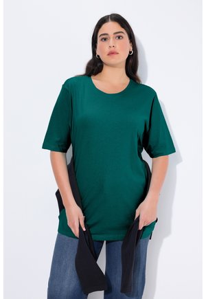 T-shirt verde a maniche corte realizzato in tessuto morbido e elastico, con scollatura rotonda e vestibilità comoda, abbinato a jeans scuri.