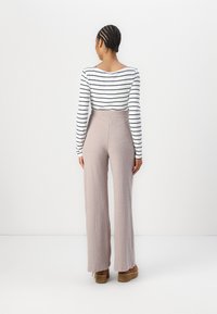 Gestreiftes langärmliges Oberteil und gerippte weite Hosen in Hellrosa. Das Outfit hat eine hohe Taille und einen strukturierten Stoff. Braune Plateau-Schuhe.