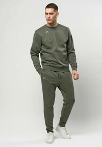 Olivengrønt sett med genser og joggebukser laget av mykt stoff. Genseren har rund hals og subtil logo. Joggebuksene har elastisk midjebånd.