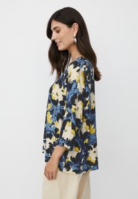 Blusa floral con estampados en azul, amarillo y crema; corte holgado, mangas tres cuartos y escote redondo. El tejido parece suave.