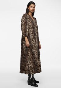 Abito maxi a stampa leopardata con scollatura a V, maniche a tre quarti e vestibilità ampia. Indossato con stivali da cowboy neri con dettagli bianchi.