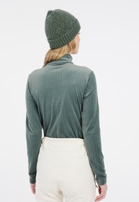 Haut vert texturé à manches longues avec un col montant, associé à un pantalon crème et un bonnet en tricot assorti.