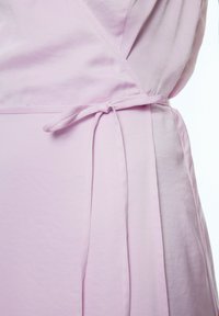Helles rosa Wickelkleid mit tailliertem Oberteil, gebundenem Taillendetail und weichem Stoff. Der Stoff wirkt glatt mit leichter Satinoptik.