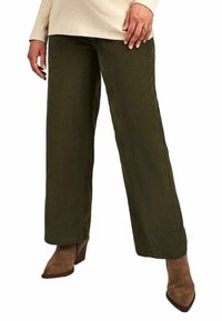 Pantaloni largi din catifea în verde măsliniu, cu fâșii verticale. Prezintă o textură netedă și o talie medie, asortați cu cizme maro cu toc.