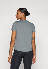 Camiseta gris de manga corta con cuello redondo, textura suave y corte holgado, combinada con leggings negros. Sin patrones ni elementos metálicos visibles.