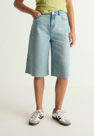Ljusblå denim culotte-shorts med rå kant, hög midja och framfickor, tillsammans med vita och grå sneakers.